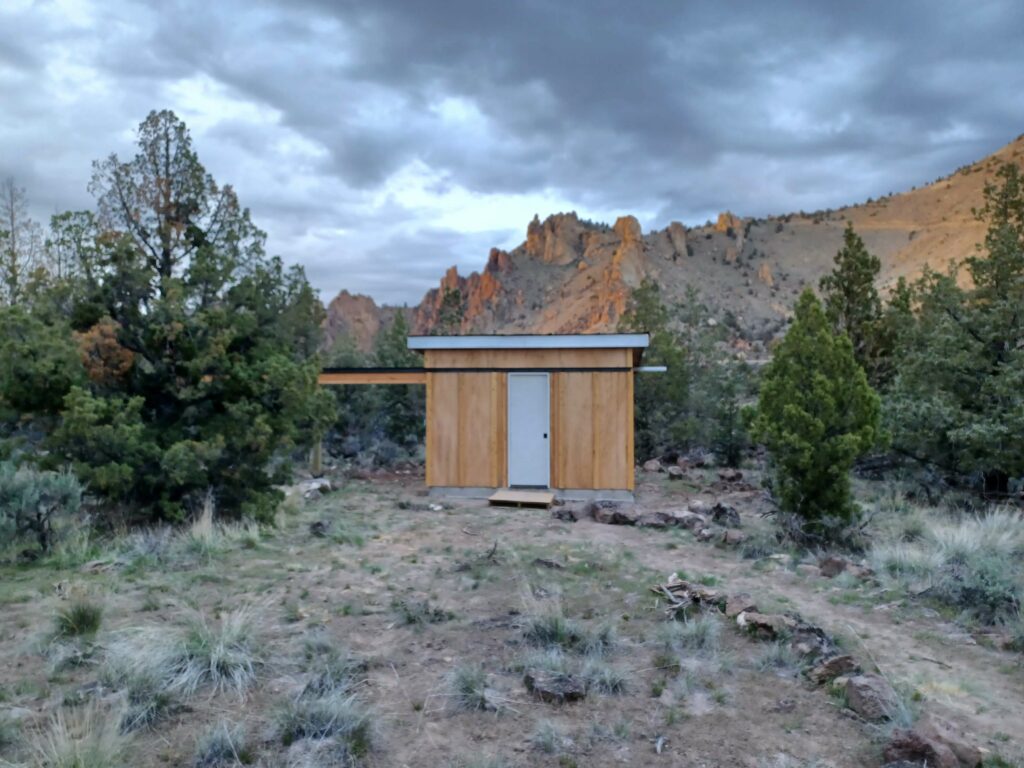 Small, square wooden observatory building in front of orange rocks at Smith Rock.