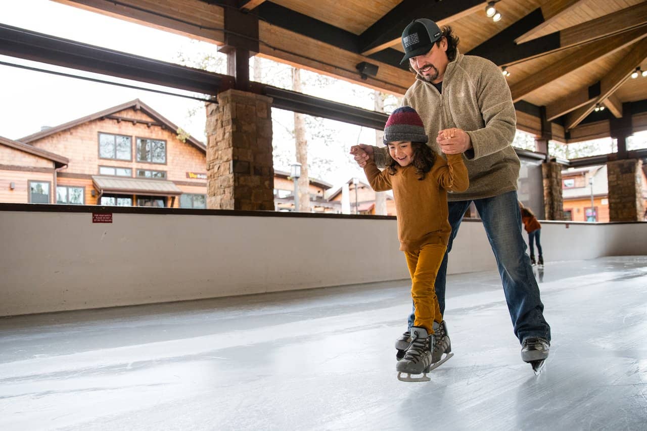 A father helping his daughter skate around the rink A father helping his daughter skate around the rink
