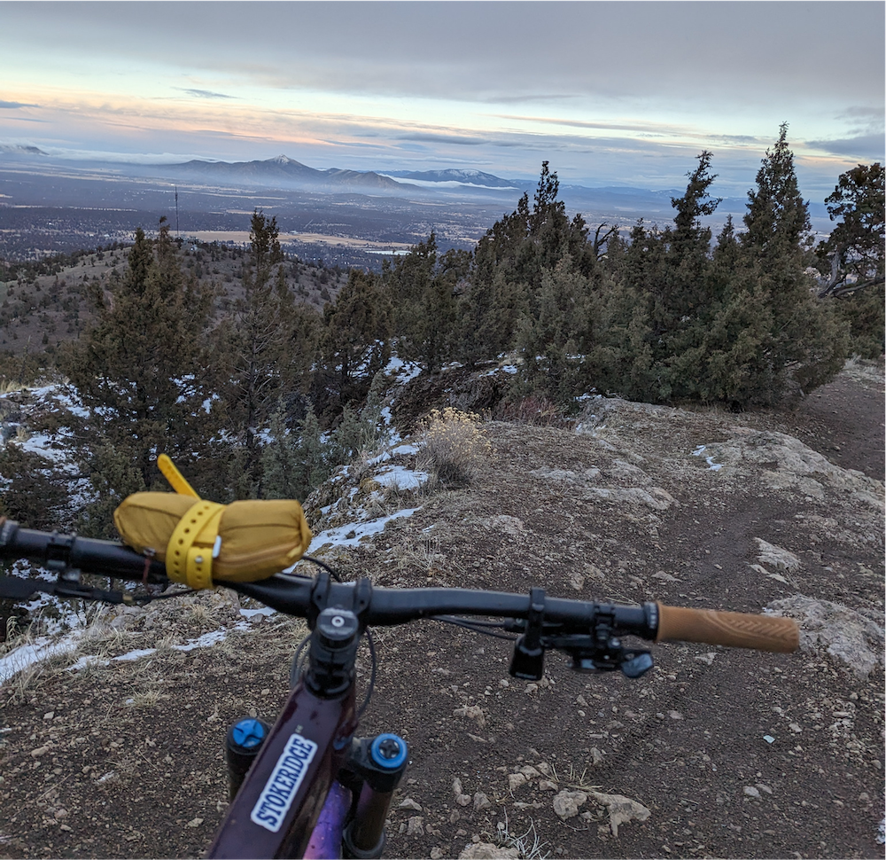 Bike handlebars overlooking cliffs of Cline Butte with sunset in sky.